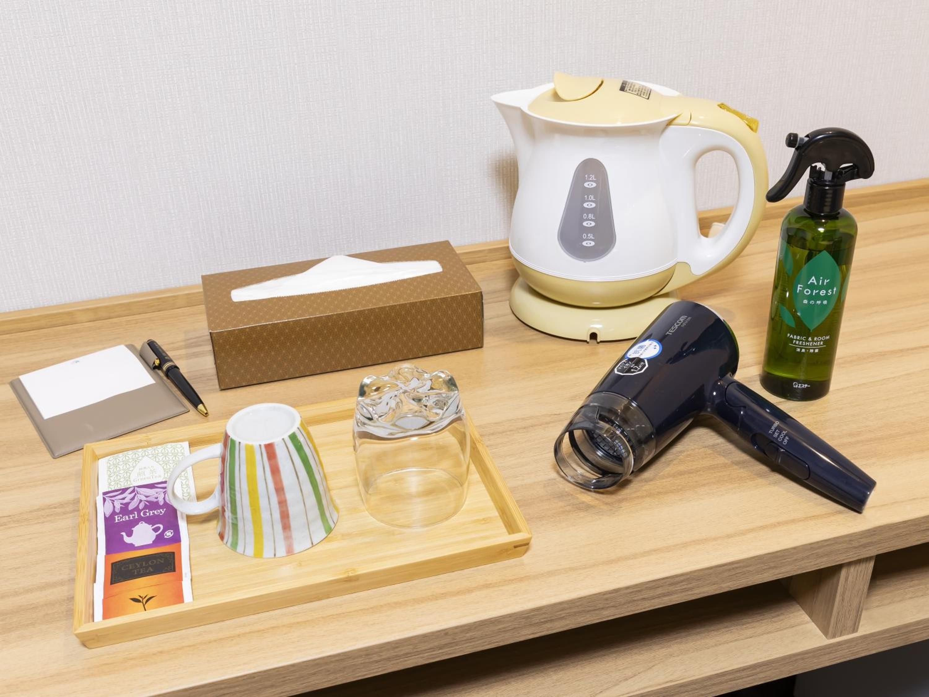 Una bandeja de madera con una caja de té, un bolígrafo, una taza, un atomizador y una tetera.