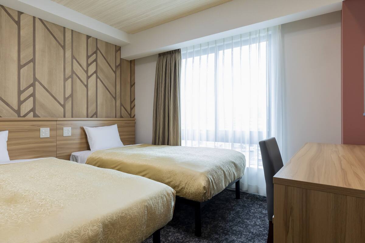 Ein Hotelzimmer mit zwei Betten, einem Schreibtisch und einem Vorhangfenster.