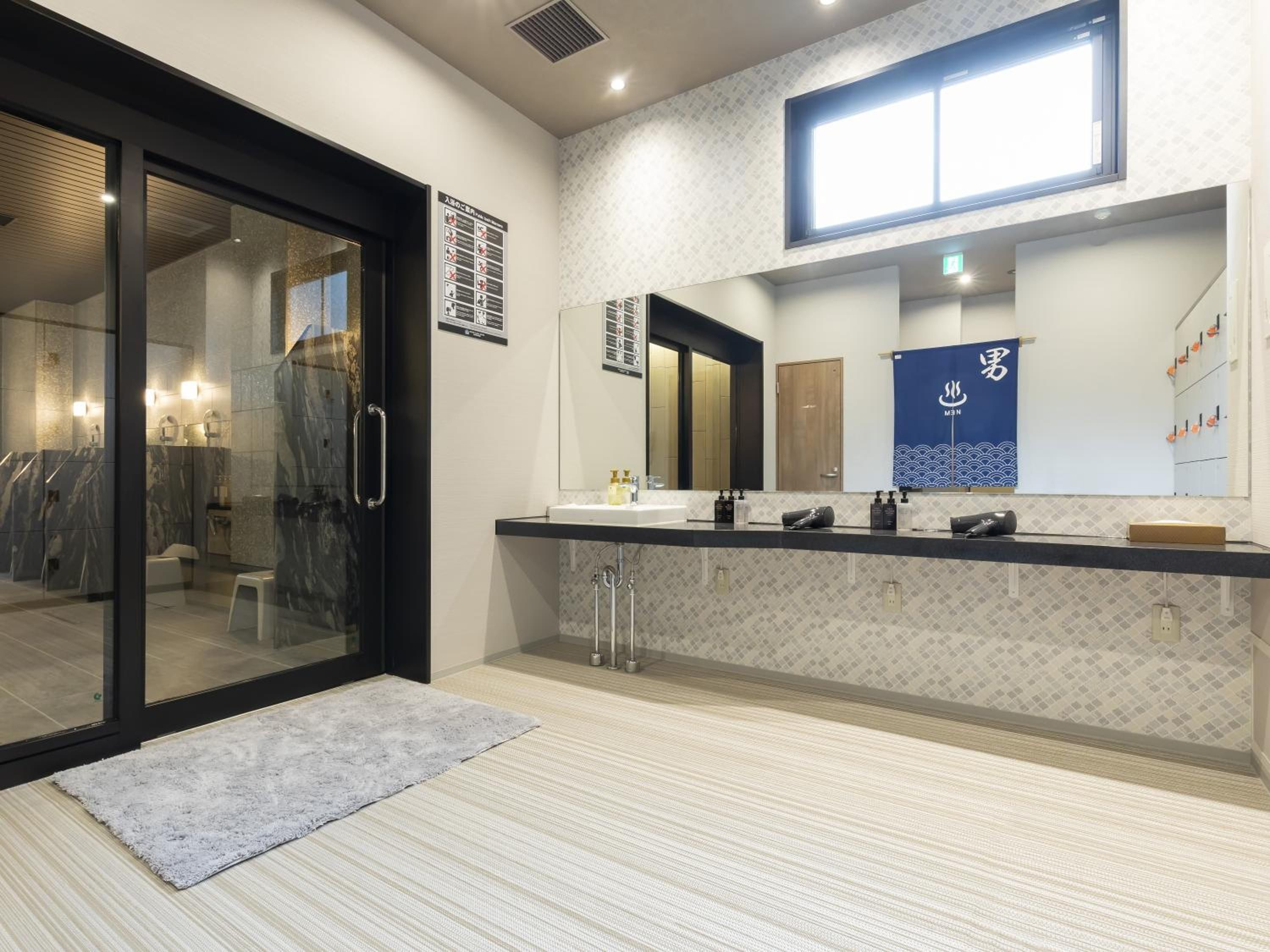 Un baño moderno con entrada de puerta de vidrio, un espejo grande y un perchero para toallas.