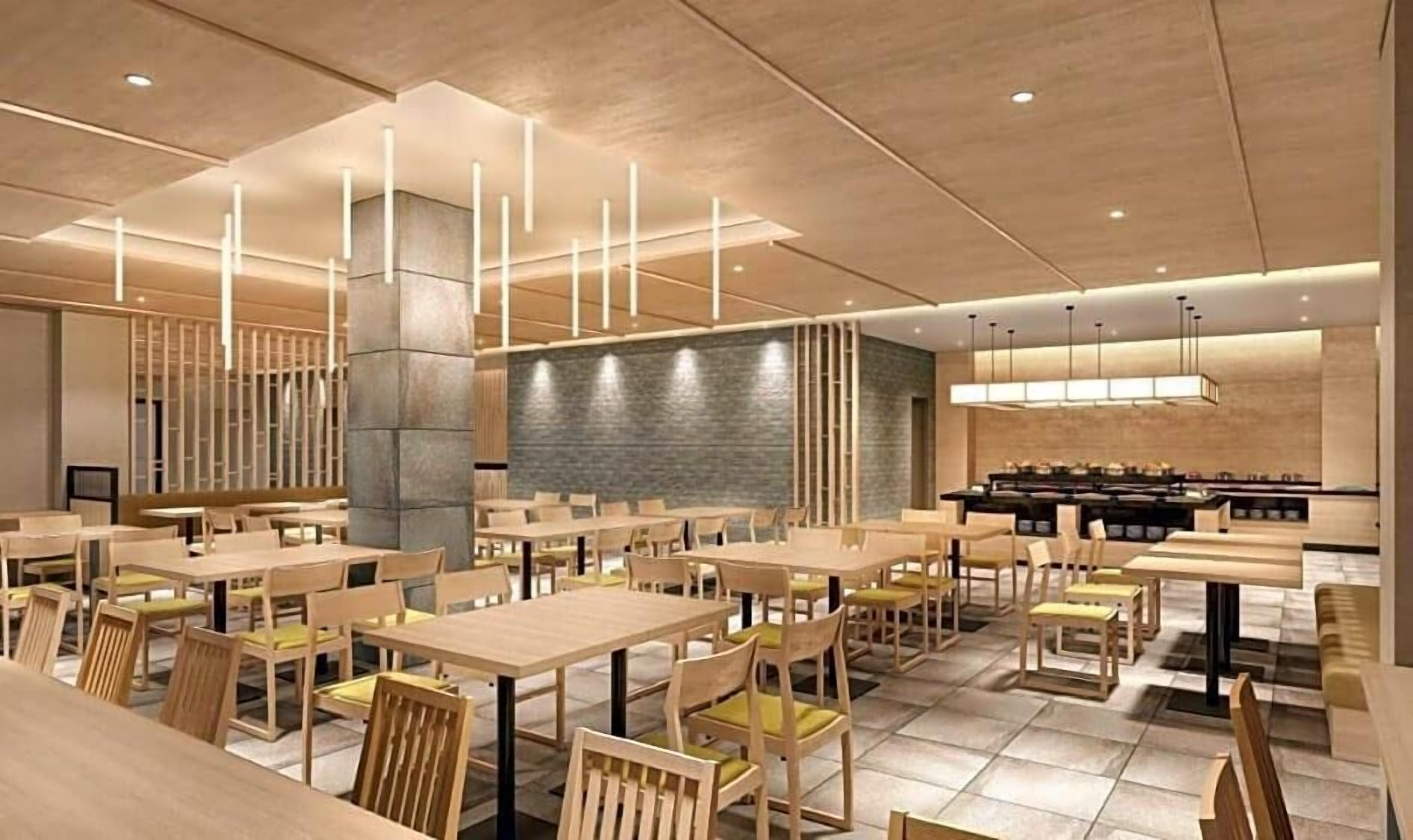 A modern restaurant with wooden tables and chairs, a stone wall, and pendant lighting.