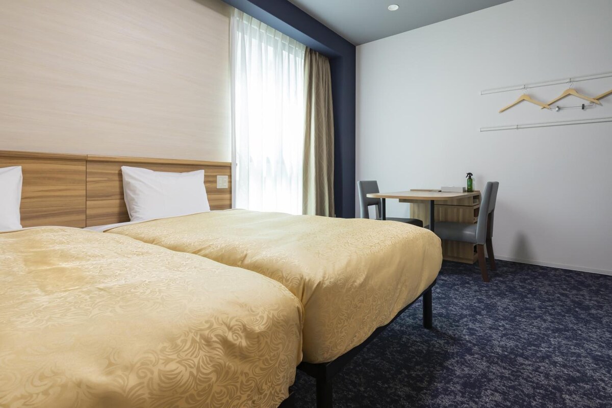 A hotel room with two beds, a desk, and a chair.