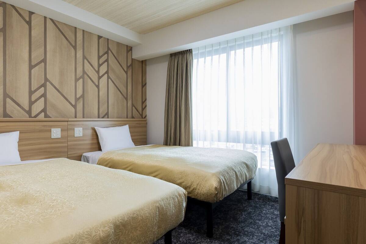 Ein Hotelzimmer mit zwei Betten, einem Schreibtisch und einem Fenster mit Vorhängen.