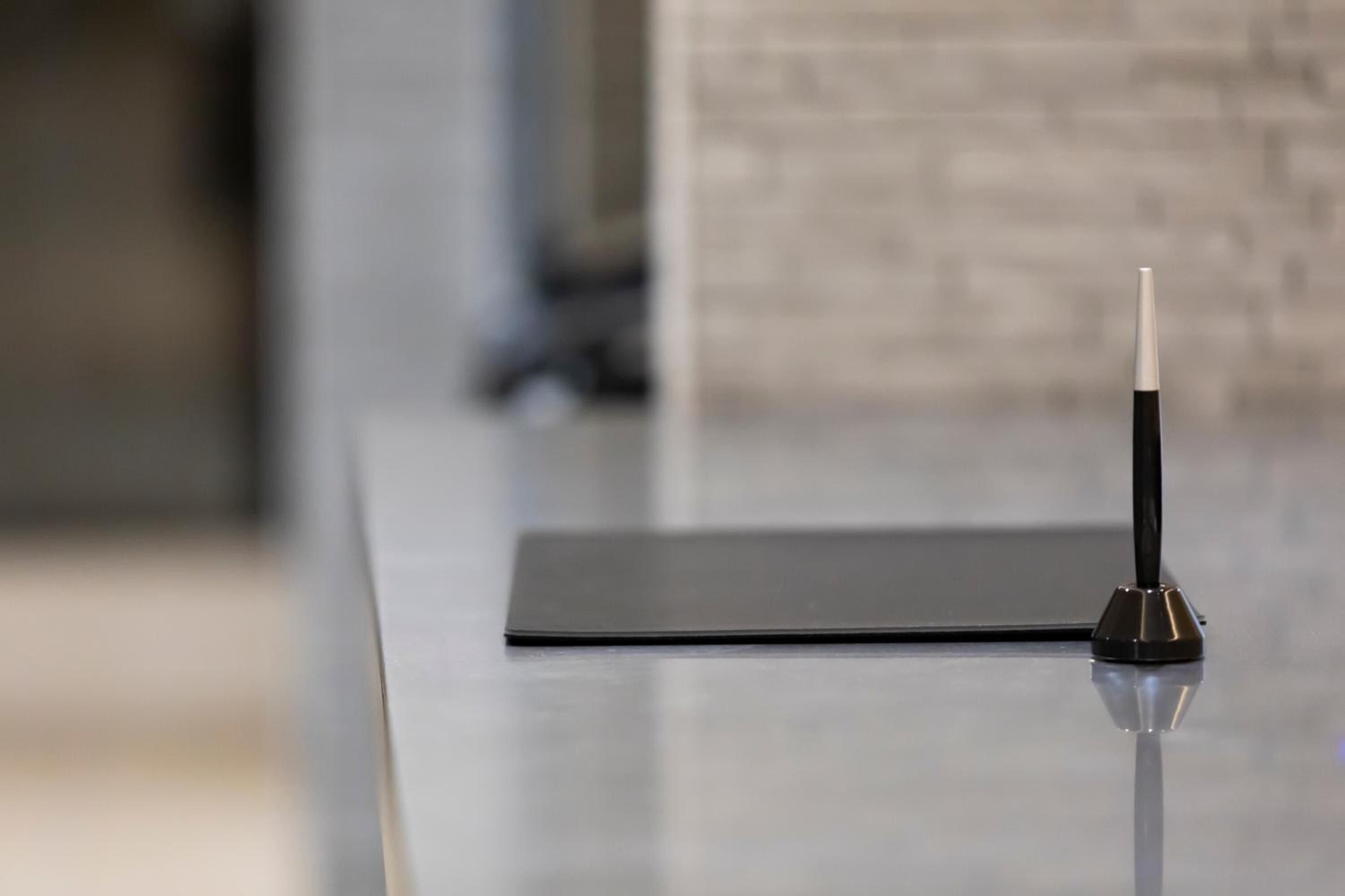 A modern, minimalist table with a sleek, black surface and a single, slender, metallic object on top.
