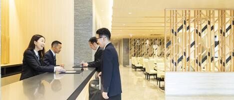 A hotel reception area with a modern design, including a reception desk, seating area, and a patterned wall.