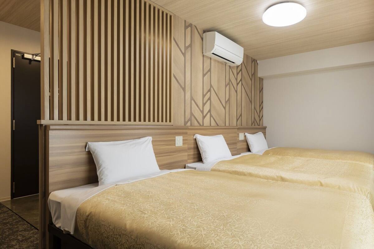 Ein Hotelzimmer mit zwei Betten, einem Holzkopfstück, einer Klimaanlage und einer Deckenleuchte.