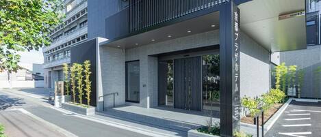 A modern hotel building with a glass facade, a covered entrance, and a parking area.