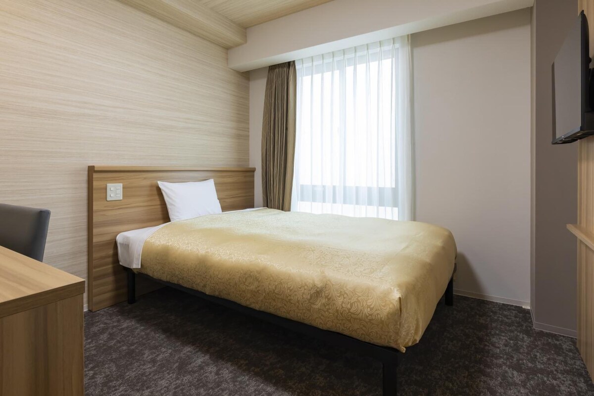 A hotel room with a bed, a desk, a chair, a television, and a window with curtains.