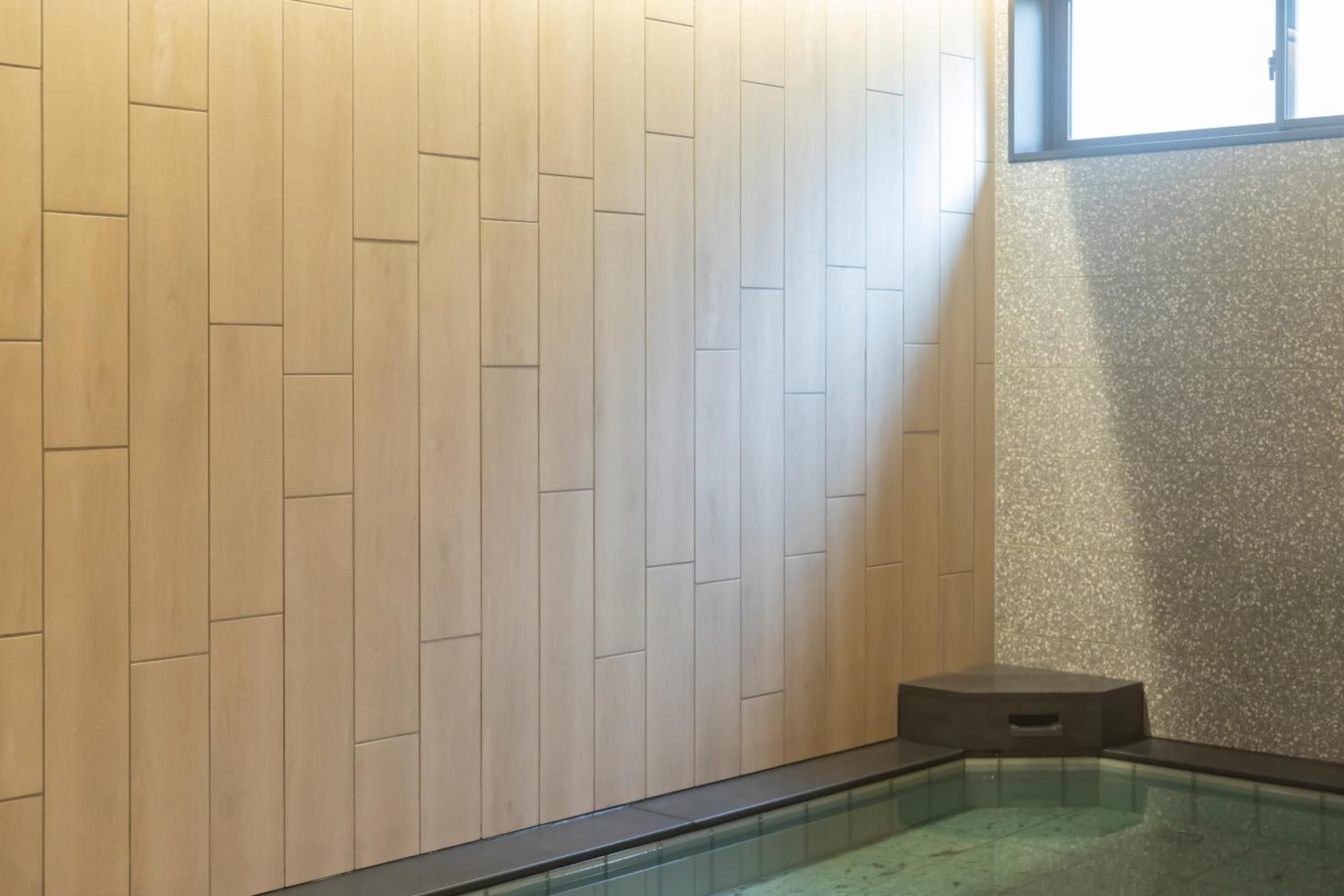 Zona de spa con pared de madera, un escalón pequeño que lleva a un jacuzzi con paredes de vidrio, y una ventana que proporciona luz natural.