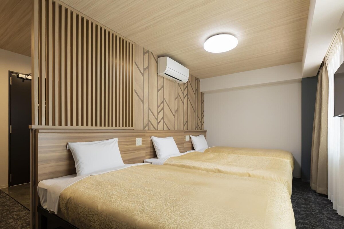 A hotel room with two beds, a wooden headboard, a wall-mounted air conditioner, and a ceiling light.