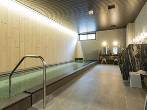 Ein modernes Badezimmer mit einem durch eine Glasscheibe abgeschirmten Pool, einer Marmorwand und einem Waschbeckenbereich.