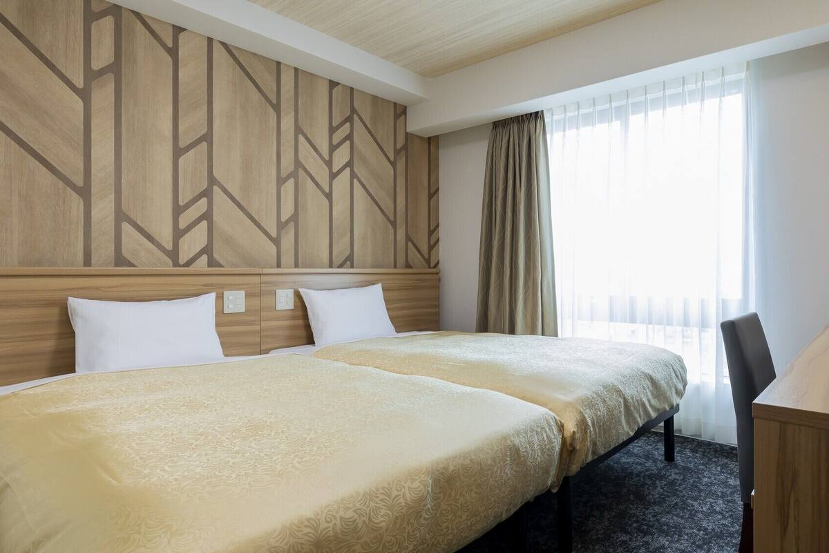 Ein Hotelzimmer mit zwei Betten, einem Schreibtisch und einem Fenster mit Vorhängen.