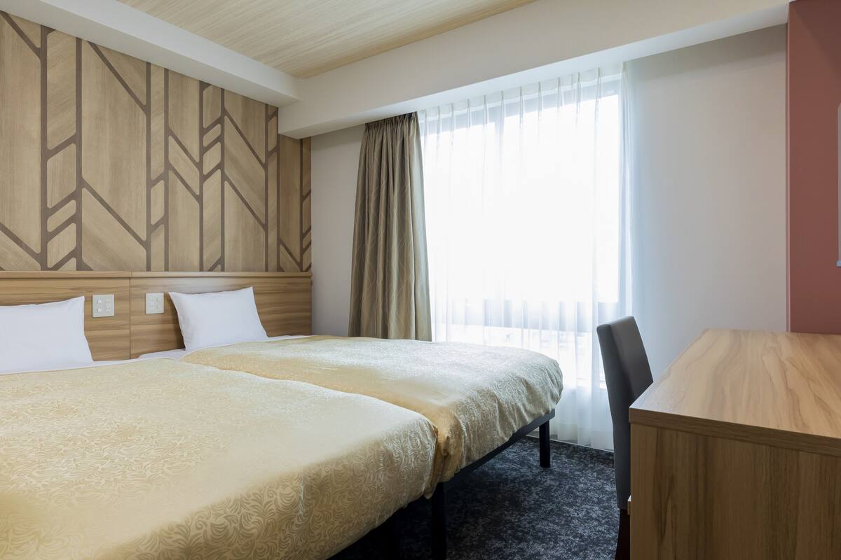 Ein Hotelzimmer mit zwei Betten, einem Schreibtisch und einem großen Fenster mit Vorhängen.