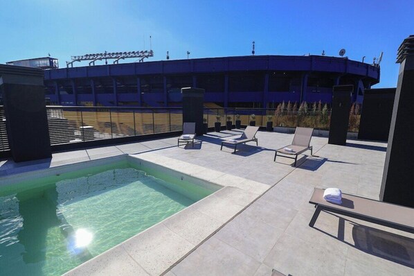 Une piscine sur le toit, avec des chaises longues et une vue sur un grand bâtiment en arrière-plan.