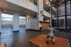 Um hall amplo com uma grande parede de vidro, uma estátua sobre uma mesa e um teto alto com vigas aparentes.
