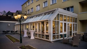 A conservatory with glass walls, outdoor seating, and a lamp post. - ANA Living Karlsruhe, Trademark Collection by Wyndham (Karlsruhe)