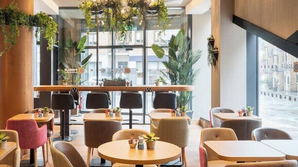 Un interno di un caffè moderno con tavoli rotondi, sedie imbottite e piante pensili.