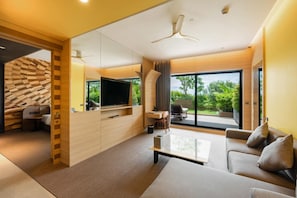 A modern living room with a flat-screen TV, a sofa, a coffee table, and a large window offering a view of greenery. - Sun and Moon Riverside Hotel (Phnom Penh)