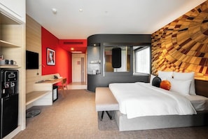 Ein modernes Hotelzimmer mit Bett, Schreibtisch, Minibar und Fernseher.