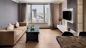 A modern hotel room with a large window offering a city view, a sofa, a coffee table, and a flat-screen TV mounted on the wall. - Kravan (Phnom Penh)