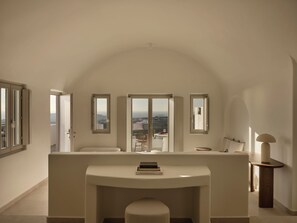 A spacious room with a large arched ceiling, a central seating area with a table, and multiple windows offering views of the landscape. - Ark Santorini (Santorini)