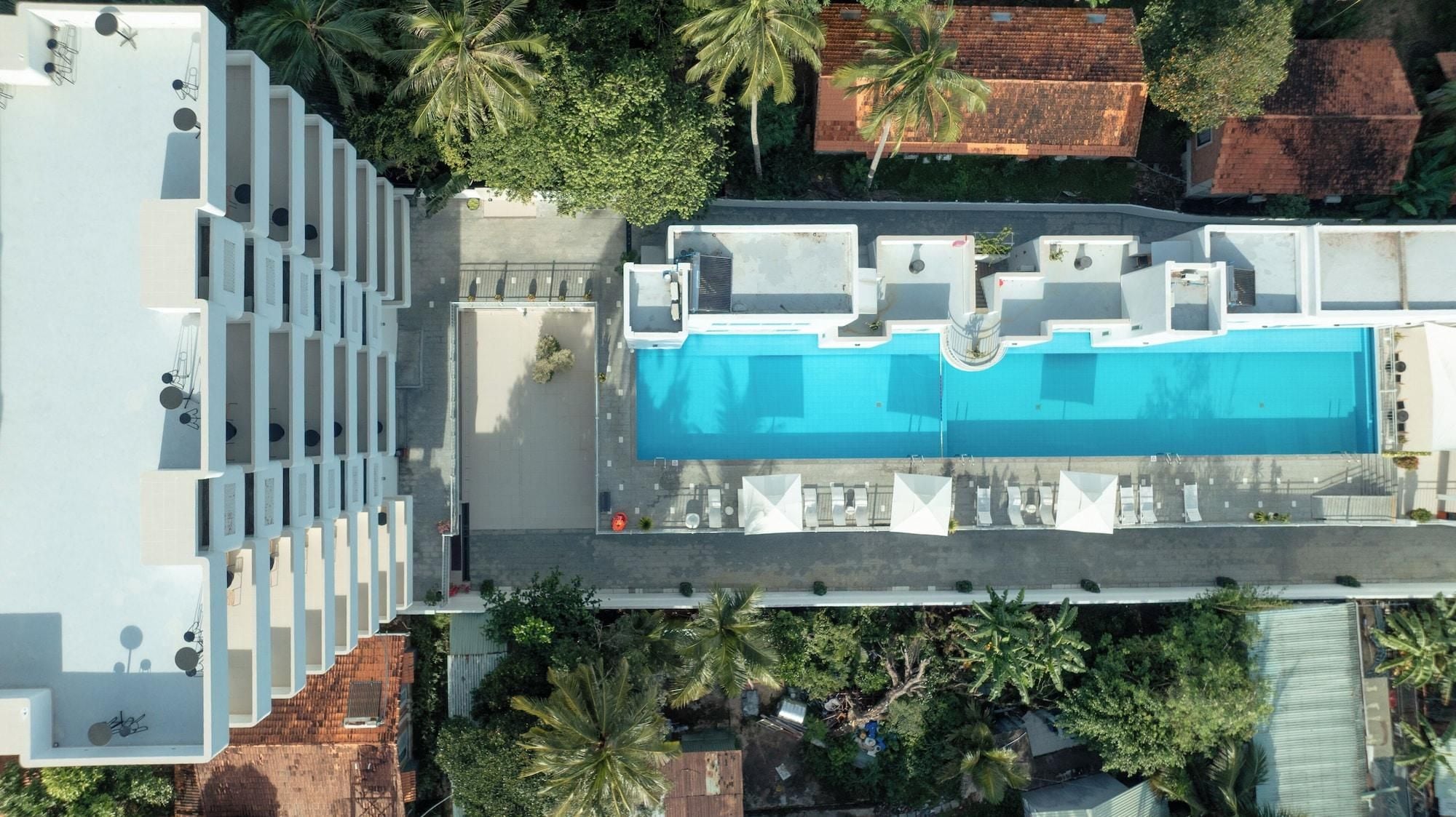 An aerial view of a hotel with a swimming pool, multiple balconies, and surrounding greenery.