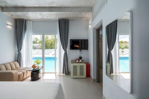 A modern hotel room with a sofa, a TV, a small table with a vase, and a view of a swimming pool. - The Up Phu Quoc (Phu Quoc)