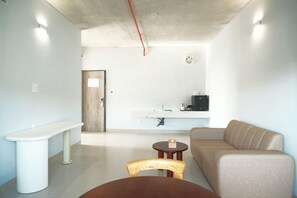 A modern living room with a sofa, a small round table, a bench, and a kitchen area with a sink and a fan. - The Up Phu Quoc (Phu Quoc)