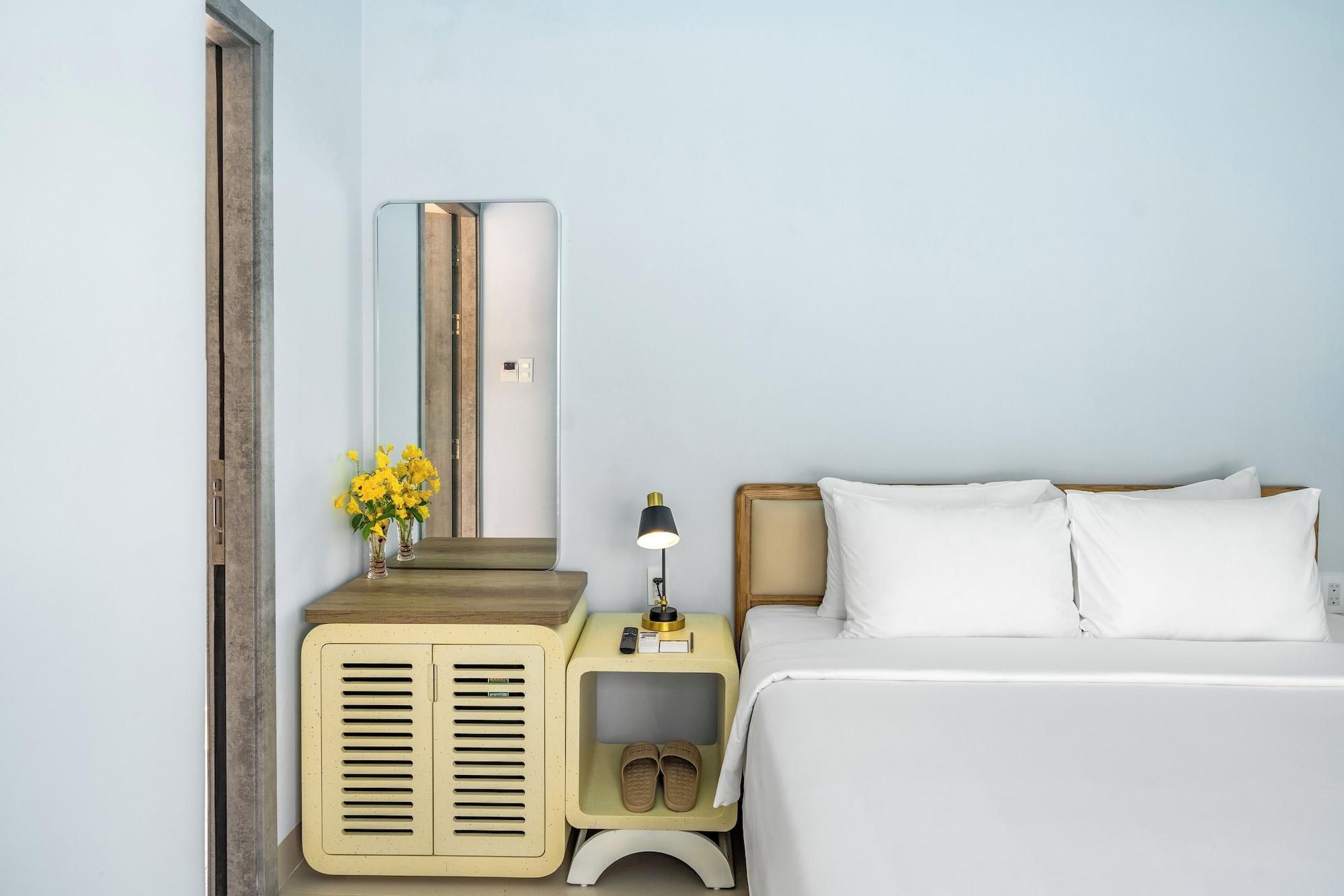 A bedroom with a bed, bedside table, lamp, and a mirror.