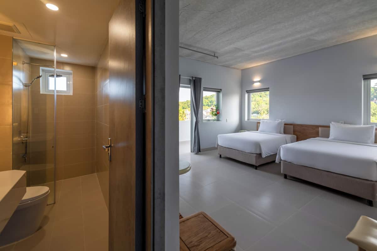 A modern hotel room with a shower, two beds, a small table, and large windows.
