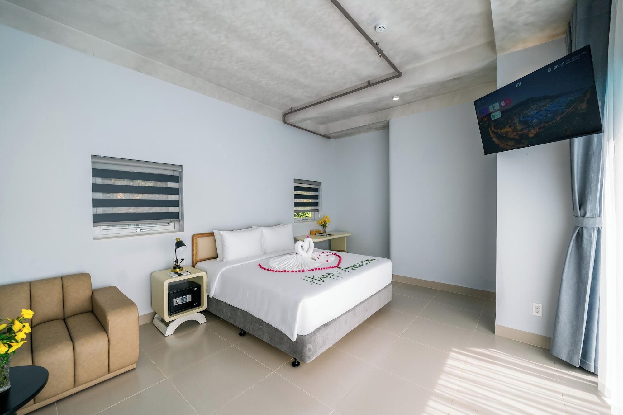 A modern hotel room with a bed, bedside table, lamp, and a TV mounted on the wall.