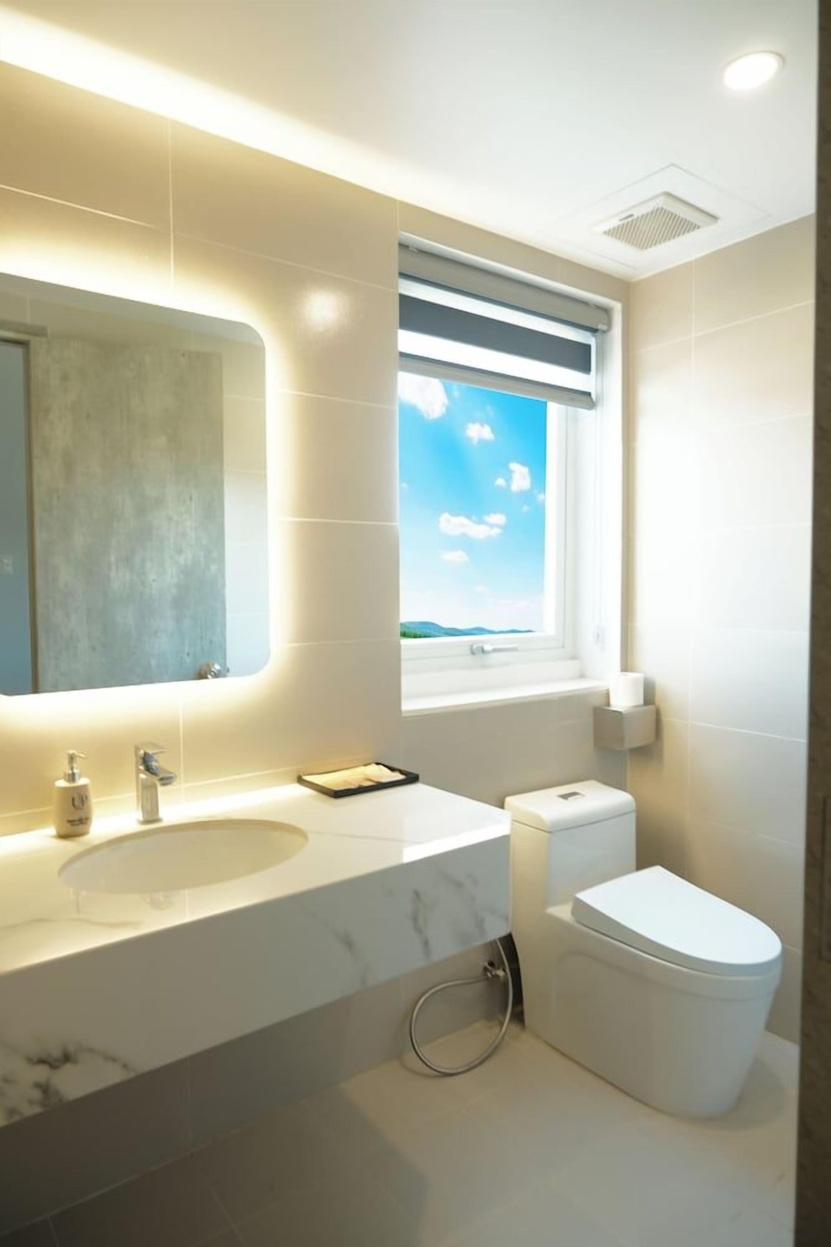 A modern bathroom with a large mirror, a sink, a toilet, and a window with a view.