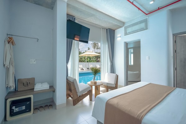 Ein Hotelzimmer mit Bett, Schreibtisch, Stuhl, einem kleinen Tisch, einem Fenster mit Blick auf einen Pool und einer Duschkabine.