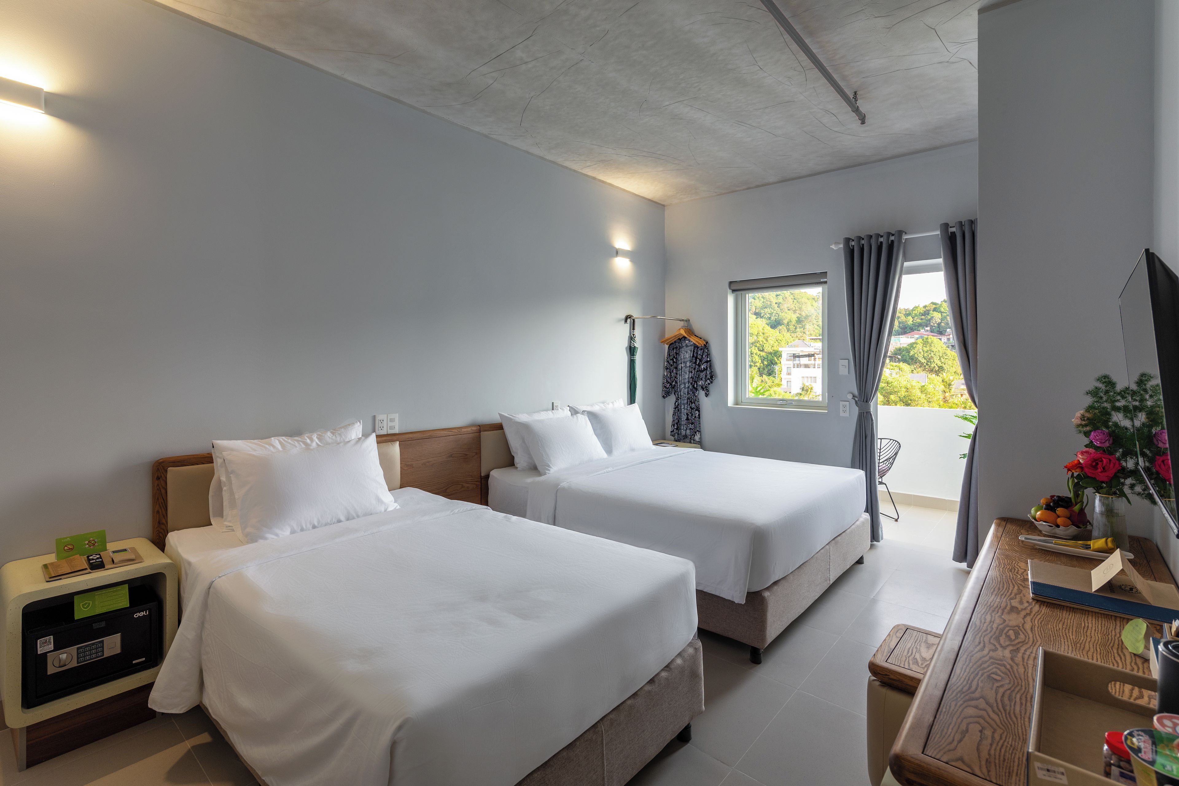 A hotel room with two beds, a desk, a chair, a TV, and a window with curtains.