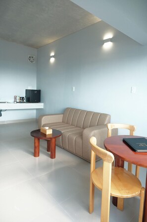 A modern living room with a sofa, two wooden chairs, a small table, and a kitchen area with a refrigerator. - The Up Phu Quoc (Phu Quoc)