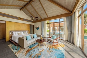 A modern hotel room with a large bed, a sofa, a coffee table, and a view of an outdoor pool area. - Fusion Resort and Villas Da Nang (Da Nang)