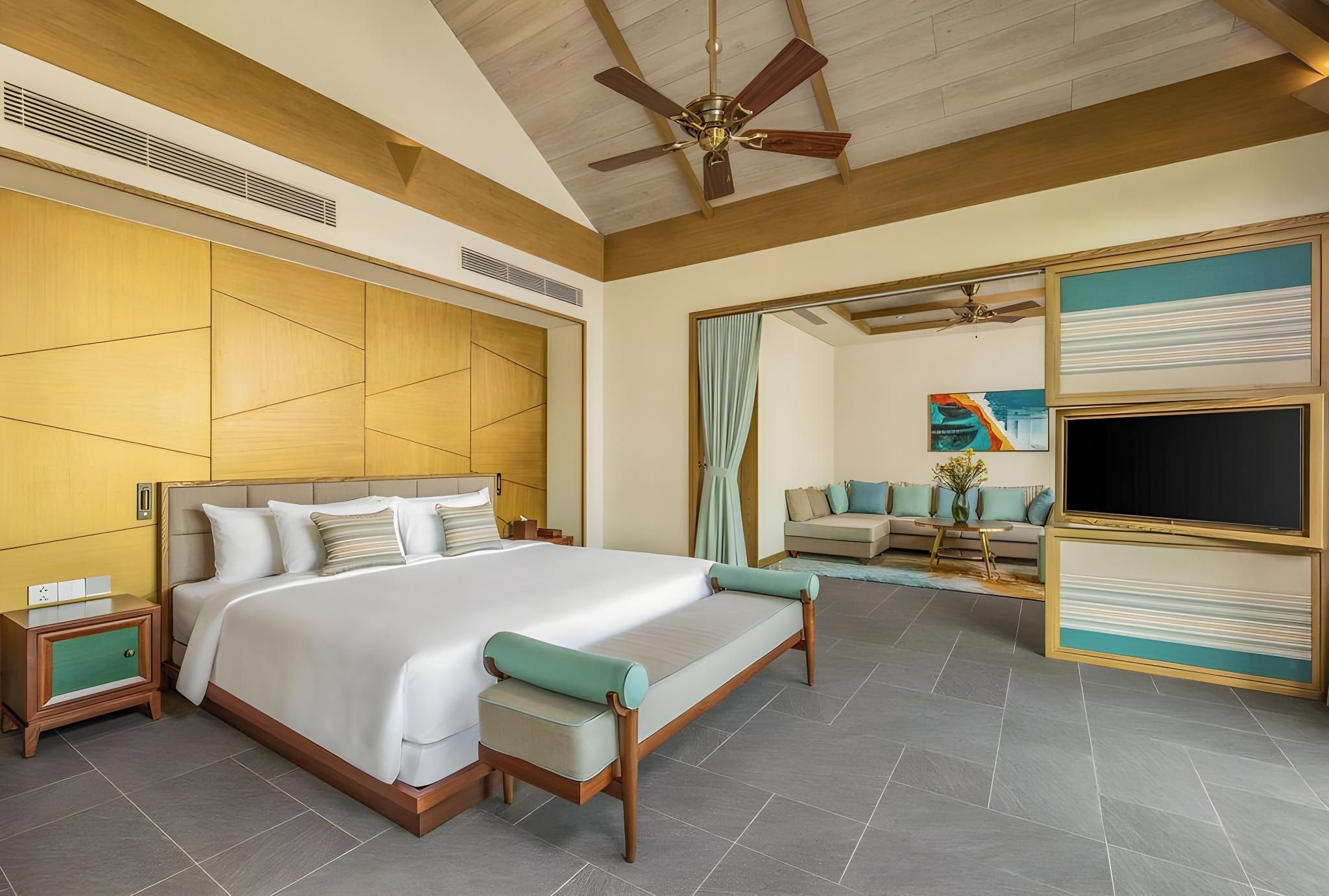 A hotel room with a large bed, a seating area, a TV, and a ceiling fan.