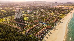 An aerial view of a coastal resort with multiple bungalow-style buildings, a central swimming pool, and a beachfront. - Fusion Resort and Villas Da Nang (Da Nang)