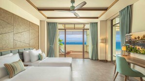 Habitació d'hotel amb dos llits, un escriptori, una cadira, un ventilador de sostre i vista a l'oceà.