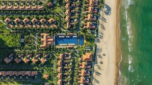 Vista aèria d'un complex turístic amb diverses edificacions de tipus bungalow, una zona de piscina central i una platja.