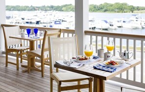 A dining area with wooden tables and chairs, breakfast items, and a view of a marina with boats. - Baron's Cove (Sag Harbor)