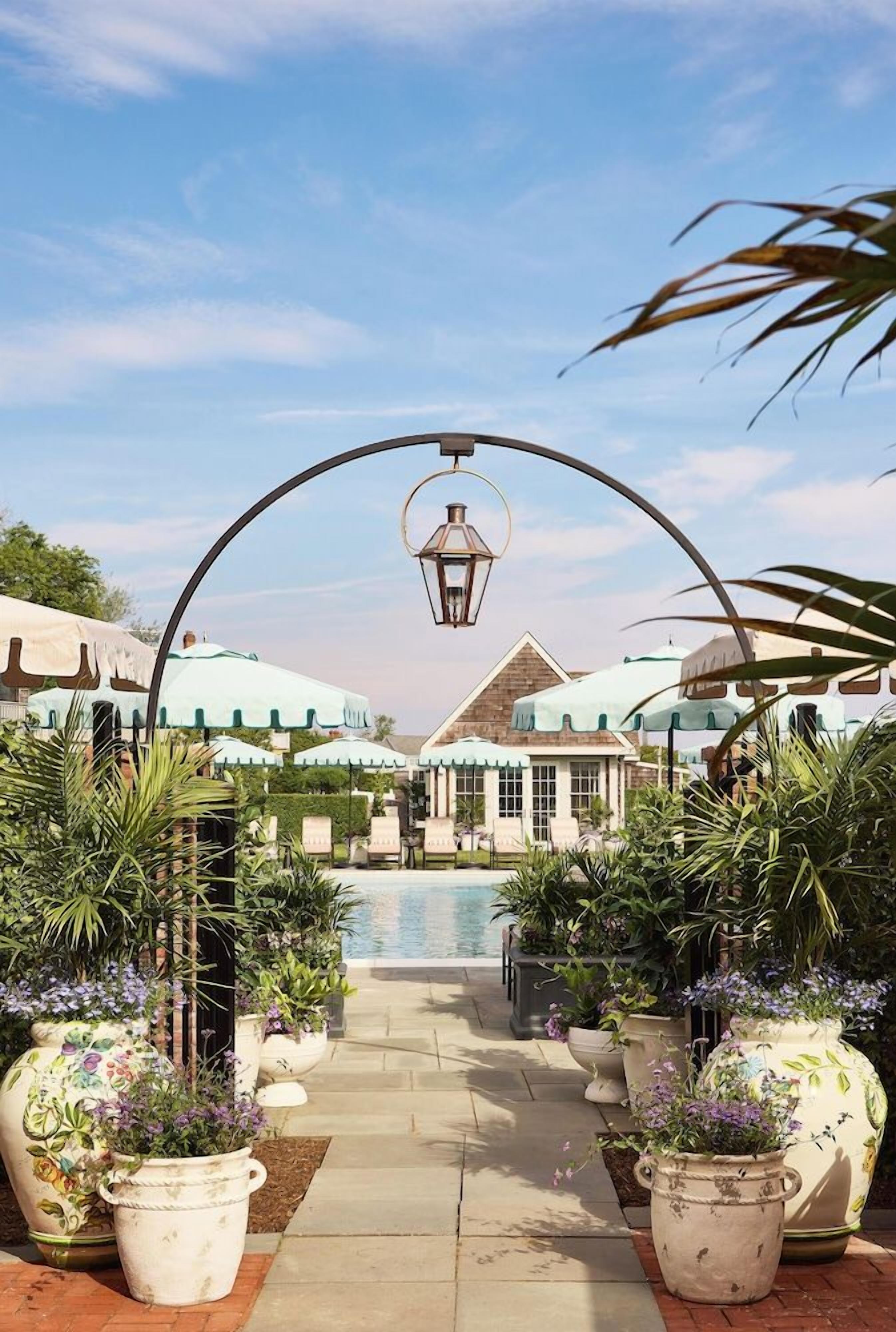 A pool area with lounge chairs, potted plants, and umbrellas.