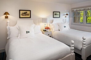 A hotel room with two white beds, a nightstand with a lamp, and framed pictures on the wall. - Baron's Cove (Sag Harbor)