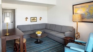 A living room with a gray sectional sofa, a round coffee table with flowers, a wooden side table, a blue armchair, and a map on the wall. - Baron's Cove (Sag Harbor)