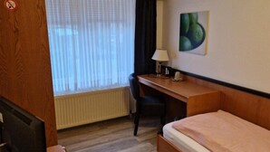 A hotel room with a wooden desk, a single bed, a chair, a TV, and a window with curtains. - Sporthotel Papenburg (Papenburg)
