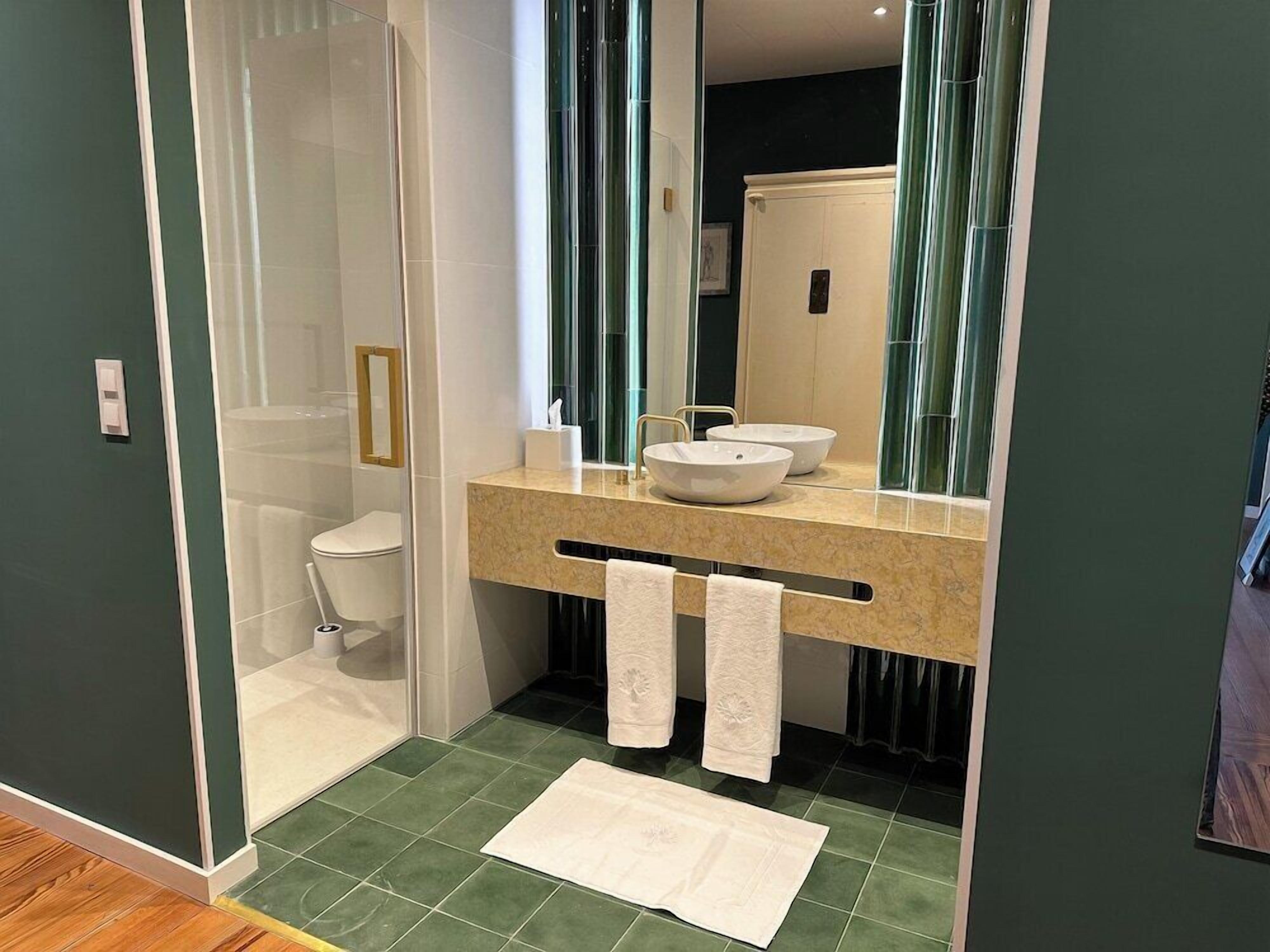 A modern bathroom with a glass-enclosed shower, a white toilet, a beige countertop with two sinks, and a mirror.