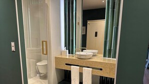 A modern bathroom with a glass-enclosed shower, a white toilet, a beige countertop with two sinks, and a mirror. - Solar dos Cantos Botanic House and Garden (Ponta Delgada)