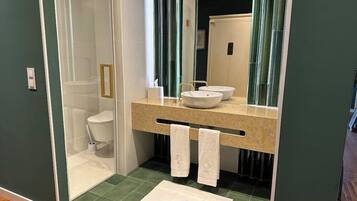 A modern bathroom with a glass-enclosed shower, a white toilet, a beige countertop with two sinks, and a mirror.