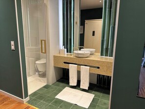 A modern bathroom with a glass-enclosed shower, a white toilet, a beige countertop with two sinks, and a mirror. - Solar dos Cantos Botanic House and Garden (Ponta Delgada)