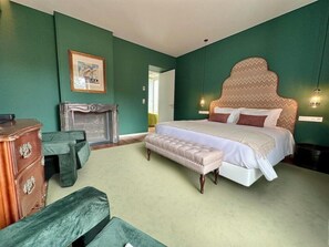 Un dormitorio con una cama grande, un banco, un aparador y una chimenea.