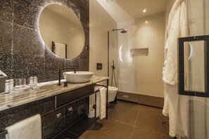 Ein modernes Badezimmer mit einem großen, ovalen Spiegel, einem Aufsatzwaschbecken, einer begehbaren Dusche und einem Handtuchhalter.